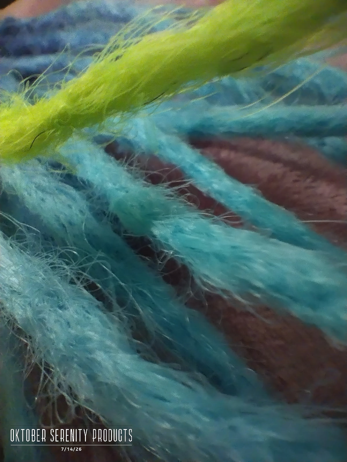 Close-up of fluffy yarn strands in bright turquoise blue, light blue, and lime green, with a vertical watermark reading 'October Serenity Products' on the right side.